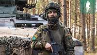 Ein Soldat steht im Kampfanzug mit Waffe vor dem Schützenpanzer Marder