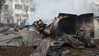 Zwei Feuerwehrleute stehen zwischen Trümmern und löschen ein Feuer