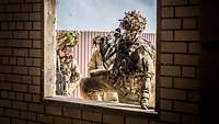 Ein Soldat steigt über das Fenster in ein Gebäude ein. Hinter ihm stehen zwei weitere Soldaten.