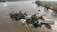 Eine Schwimmschnellbrücke mit Soldaten und Militärfahrzeugen fährt auf einem Fluss