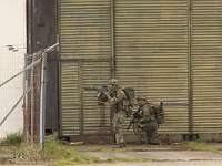 Von Gebäude zu Gebäude Zwei bewaffnete Soldaten stehen und hocken sichernd vor einem Hangartor.