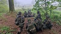 Zwei Soldaten stehen in einer Stellung mit ihren Gewehren. Andere Militärangehörige beobachten sie.