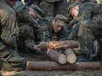 Mehrere Soldaten knien auf dem Boden und bauen ein Gestell aus Holzstämmen