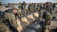Mehrere Soldaten stehen an einem Schlauchboot und bauen dieses auf