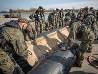 Mehrere Soldaten stehen an einem Schlauchboot und bauen dieses auf