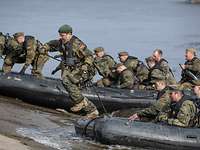 Zwei Schlauchboote mit mehreren Soldaten an einer Rampe im Wasser, ein Soldat springt aus dem Boot