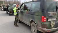 Ein Soldat steht seitlich zu einem Fahrzeug und kontrolliert dabei die Fahrzeugpapiere