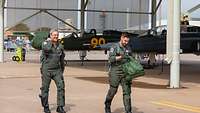 Zwei Soldaten in Fliegerkombi und mit Taschen gehen an mehreren Flugzeugen vorbei.