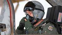 Ein Soldat mit Helm sitzt in einem Cockpit und hat beide Hände an der Sauerstoffmaske