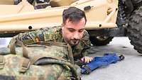 Ein Mann mit einem Rucksack und einer G36 Bluegun kriecht unter einem Fahrzeug her
