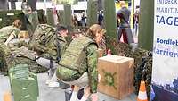 Zwei Männer mit Weste, einer mit Rucksack, stehen gebückt und greifen je nach zwei grauen Kisten.