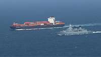 Ein Kriegsschiff fährt neben einem Containerschiff