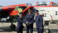 Drei Soldaten geben sich die Hand vor einem Kampfjet.