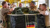 Mehrere Soldaten stehen mit Brigadegeneral Gräfe um eine gepackte Hilfsgüterpalette.