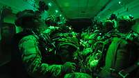 Fallschirmspringer sitzen mit angelegter Sprungausrüstung im Luftfahrzeug bei grünem Licht 