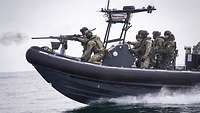 Soldaten fahren in einem Speedboot und schießen mit einem schweren Maschinengewehr M2 QCB