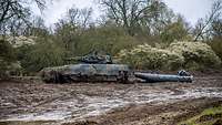 Ein Schützenpanzer Puma zieht ein Motorboot über einen Weg voller Matsch.