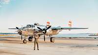 Ein Mann in Uniform steht vor einem alten Propellerflugzeug