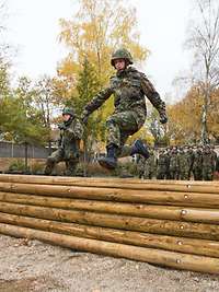 Zwei Soldaten auf der Hindernisbahn, weitere Soldaten sehen im Hintergrund zu
