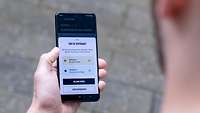 Ein Mann hält ein Handy in der linken Hand mit der geöffneten App „Meine Reserve“