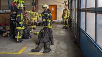 Ein Mädchen in Feuerwehr-Schutzkleidung zieht in einer Halle einen Dummy-Körper über den Boden