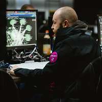 Ein Mann mit einem Patch der Telekom auf dem Arm sitzt vor Computerbildschirmen