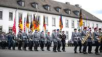 Soldatinnen und Soldaten marschieren in Uniform und tragen Instrumenten und Fahnen