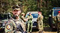 Hinter einem bewaffneten Soldaten unterhalten sich mehrere Soldaten verschiedener Nationen miteinander.