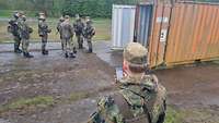 Ein Soldat blickt auf ein Handy. Vor im stehen weitere Militärangehörige.