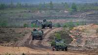 Drei kleine Militärfahrzeuge fahren hintereinander auf einem sandigen Weg