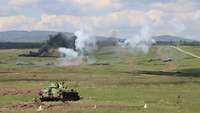Ein Schützenpanzer steht auf einer Wiese, vor ihm weiße und schwarze Rauchwolken