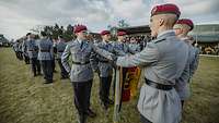 Mehrere Soldaten stehen auf einer Wiese und sprechen mit der linken Hand auf der Bundeswappenfahne