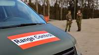 Ein grünes Fahrzeug mit der Beschriftung „Range Control“. Dahinter unterhalten sich zwei Soldaten.