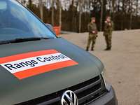 Ein grünes Fahrzeug mit der Beschriftung „Range Control“. Dahinter unterhalten sich zwei Soldaten.