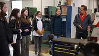 Several girls standing in a workshop looking at a man who is explaining something.
