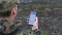 Ein Soldat blickt auf ein Smartphone