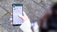 Eine Frau hält ihr Smartphone mit der geöffneten App "Meine Reserve" in der Hand