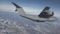 Ein graues Propellerflugzeug betankt einen Kampfjet mithilfe eines langen Schlauches in der Luft
