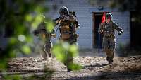 Mehrere Soldaten stürmen mit vorgehaltenen Waffen über einen Sandweg.