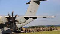 Zahlreiche Soldaten betreten mit Fallschirmen ein Flugzeug über die geöffnete Heckrampe.