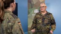 Eine Soldatin und ein Soldat stehen sich an einem Tisch gegenüber und sprechen miteinander.
