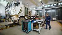 Zwei Personen stehen in einer Halle vor Werkzeugen, neben ihn ein Berge- und Abschleppfahrzeug Bison