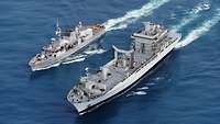A gray warship and a bigger grey ship at sea.