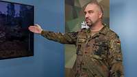 Ein Soldat steht in einem Studio während eines Interviews und zeigt auf einen Bildschirm