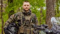 Ein Soldat steht mit seinem Motorradhelm in der Hand neben seinem Motorrad