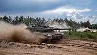 Ein Panzer fährt schnell über Übungsgelände, Sand wirbelt auf