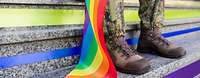 Eine Soldatin sitzt auf einer bunt beklebenden Treppe und hält eine Regenbogenflagge