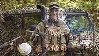 Ein Soldat steht vor einem getarnten Fahrzeug mit einer Mikro-Aufklärungsdrohne in der Hand. Der Soldat ist auch getarnt.