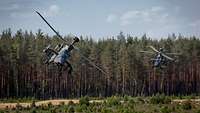 Zwei Hubschrauber fliegen sehr tief auf einer Freifläche.