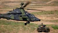 Ein Hubschrauber fliegt im Gefecht über einem fahrenden Schützenpanzer.
